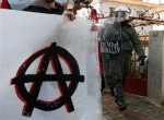 Police walk behind of anarchists' banner during a rally in the town of Amfissa, about 200 kilometers (125 miles) northwest of Athens on Wednesday, Jan. 20, 2010. A court in the small town of Amfissa postponed until Friday the trial of two policemen over a teenager's fatal shooting that sparked riots across Greece in December 2008. Minor clashes broke out when police fired tear gas at a group of some 200 mostly anarchist protesters who marched from the court house to a prison complex just outside Amfissa.